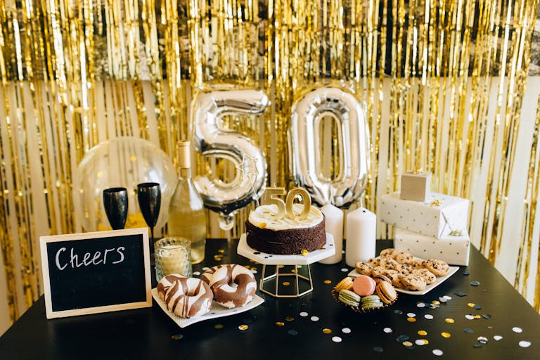 Stylish 50th birthday party setup with cake, balloons, gifts, and champagne amidst golden decorations.